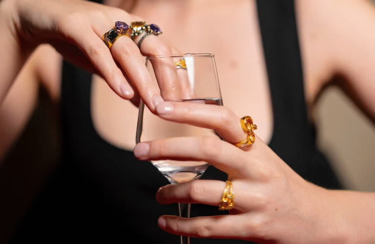 A woman wearing multiple colorful gemstone rings while holding a glass, showcasing elegance and style — perfect for Best Gemstone Jewellery Gifts Under in India.