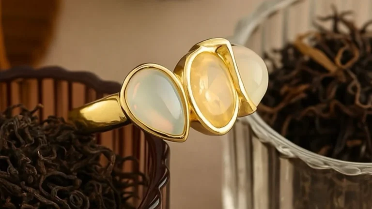 A close-up of a gold ring featuring three polished gemstone cabochons in soft pastel tones, displayed elegantly against a decorative background.